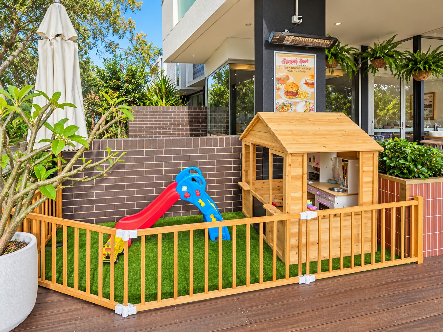 Sweet Spot’s fenced kids play area with a wooden playhouse, colourful slide and green synthetic grass